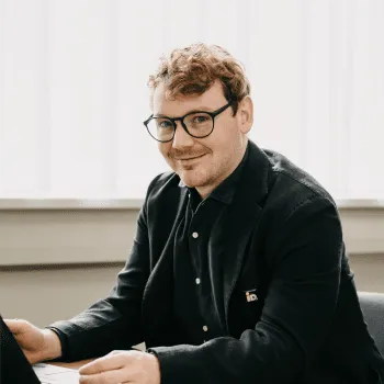 Porträt von Thomas Pletzer, Co-Geschäftsführer von iDM Energiesysteme, mit Brille und dunklem Sakko in hellem Raum.